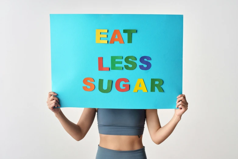a woman holds up a sign with the words eat less sugar on it