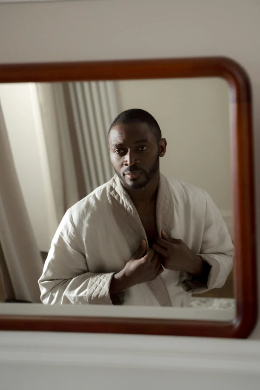 a black man in a bathrobe is shown in the reflection of a bathroom mirror