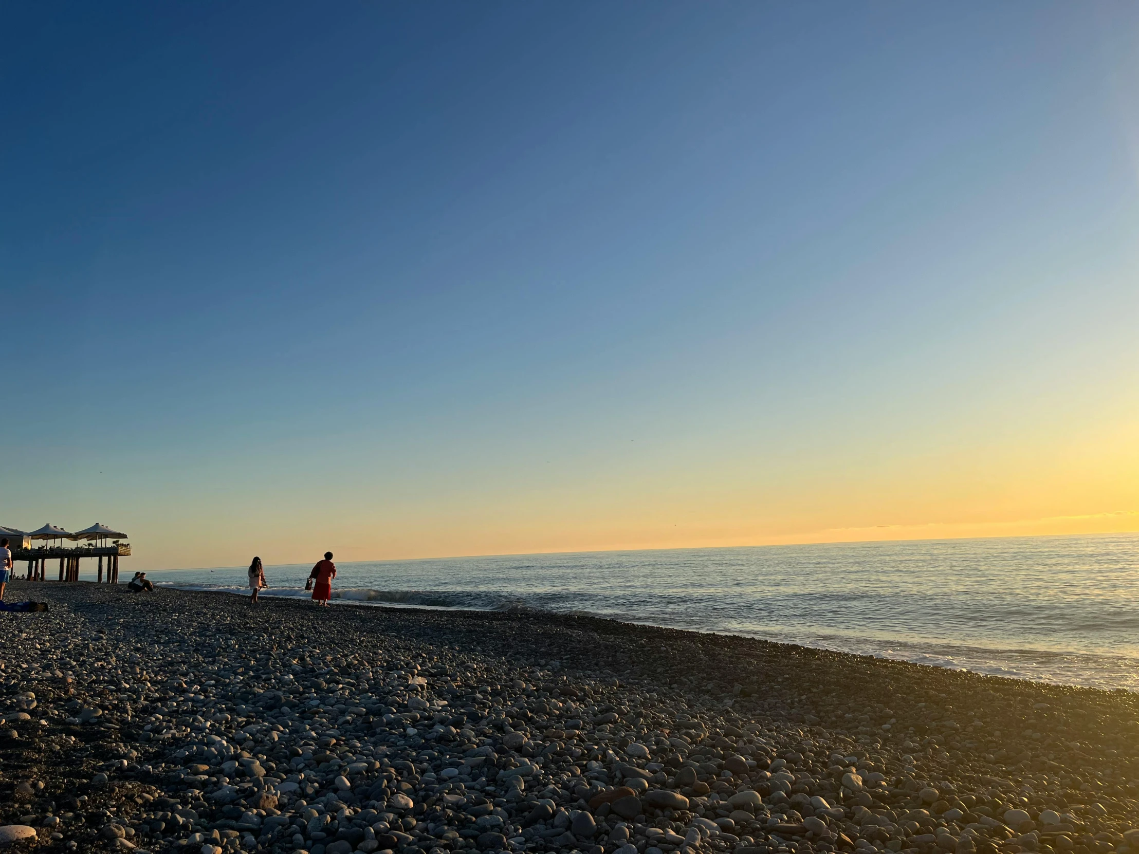 two people standing at the beach as the sun sets