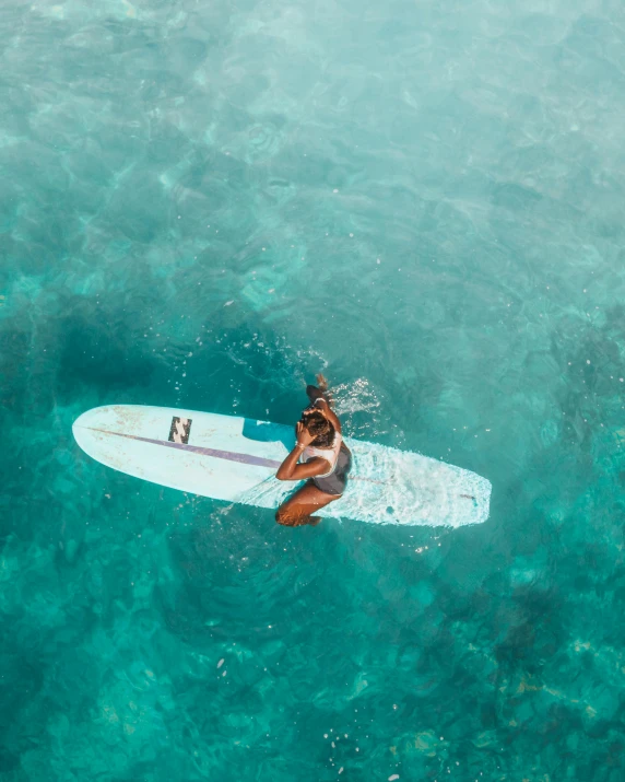 woman sitting on surf board in crystal blue water