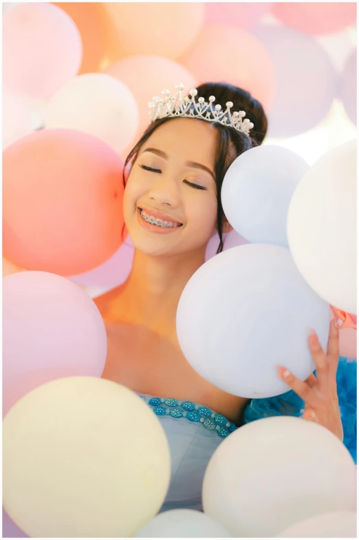 a girl wearing a tiara holding balloons and smiles