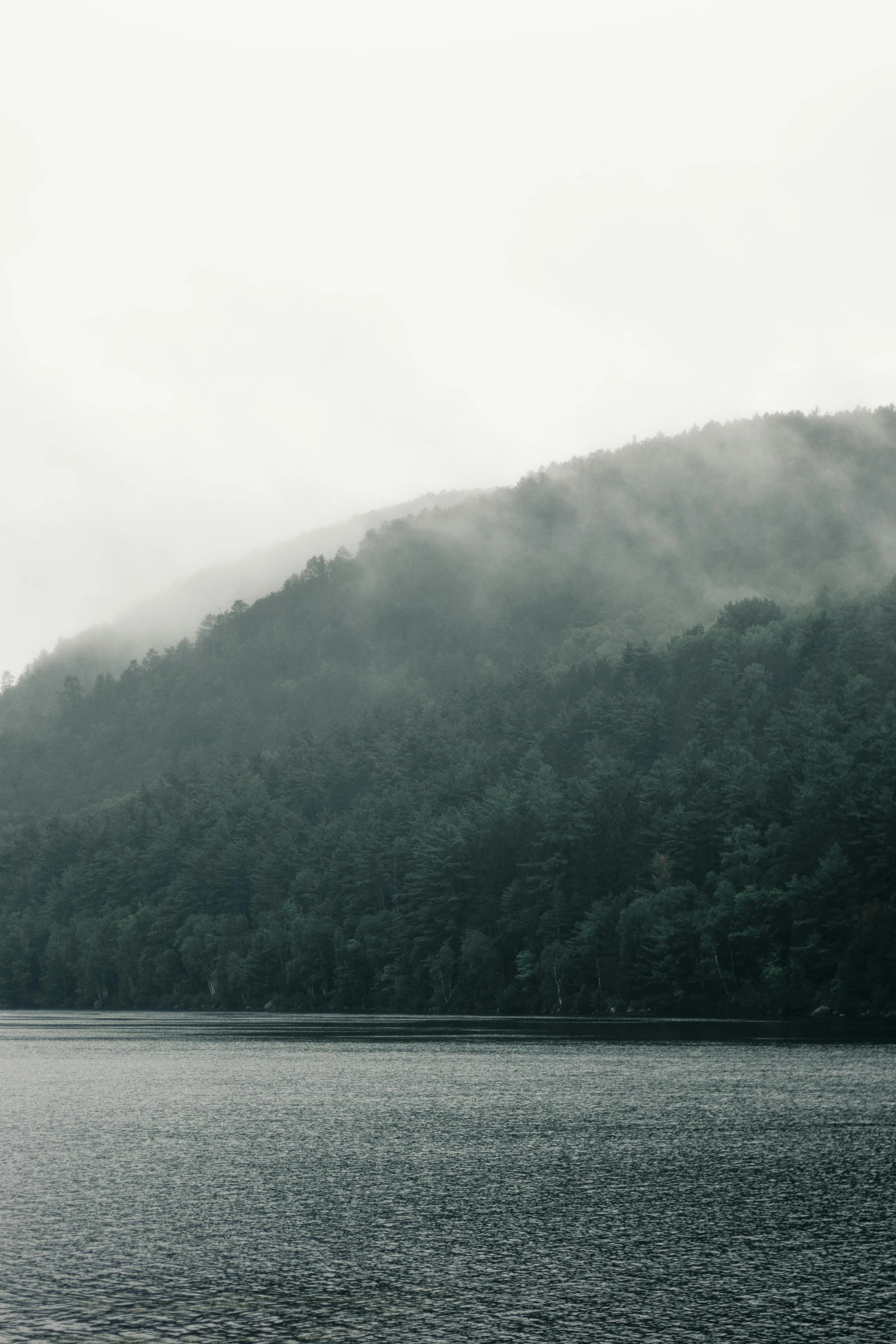 fog rising over the hillside on top of a lake