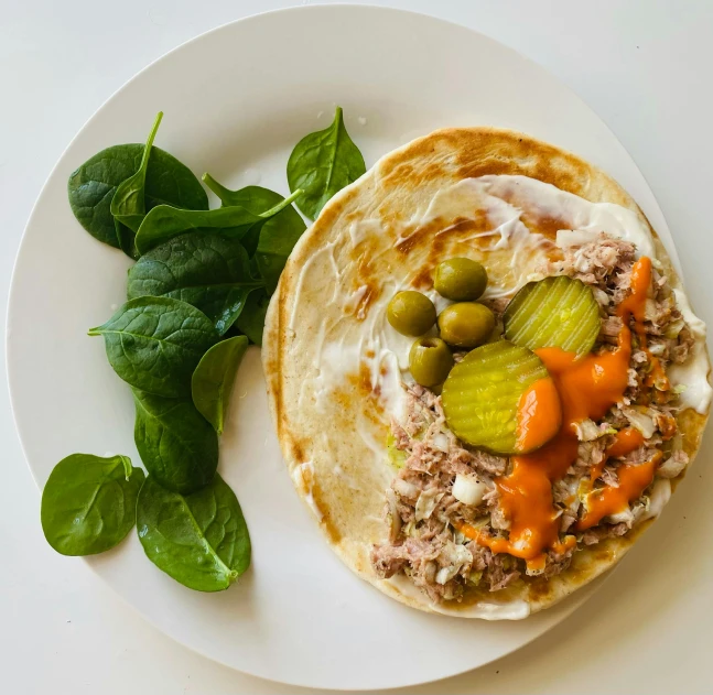 a plate has a meal consisting of a flatbread, meat and vegetables