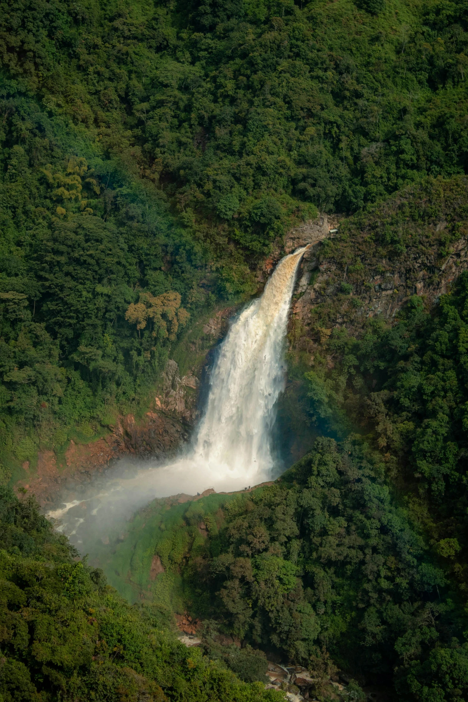 waterfall with rainbow coming out of the water near a green hill