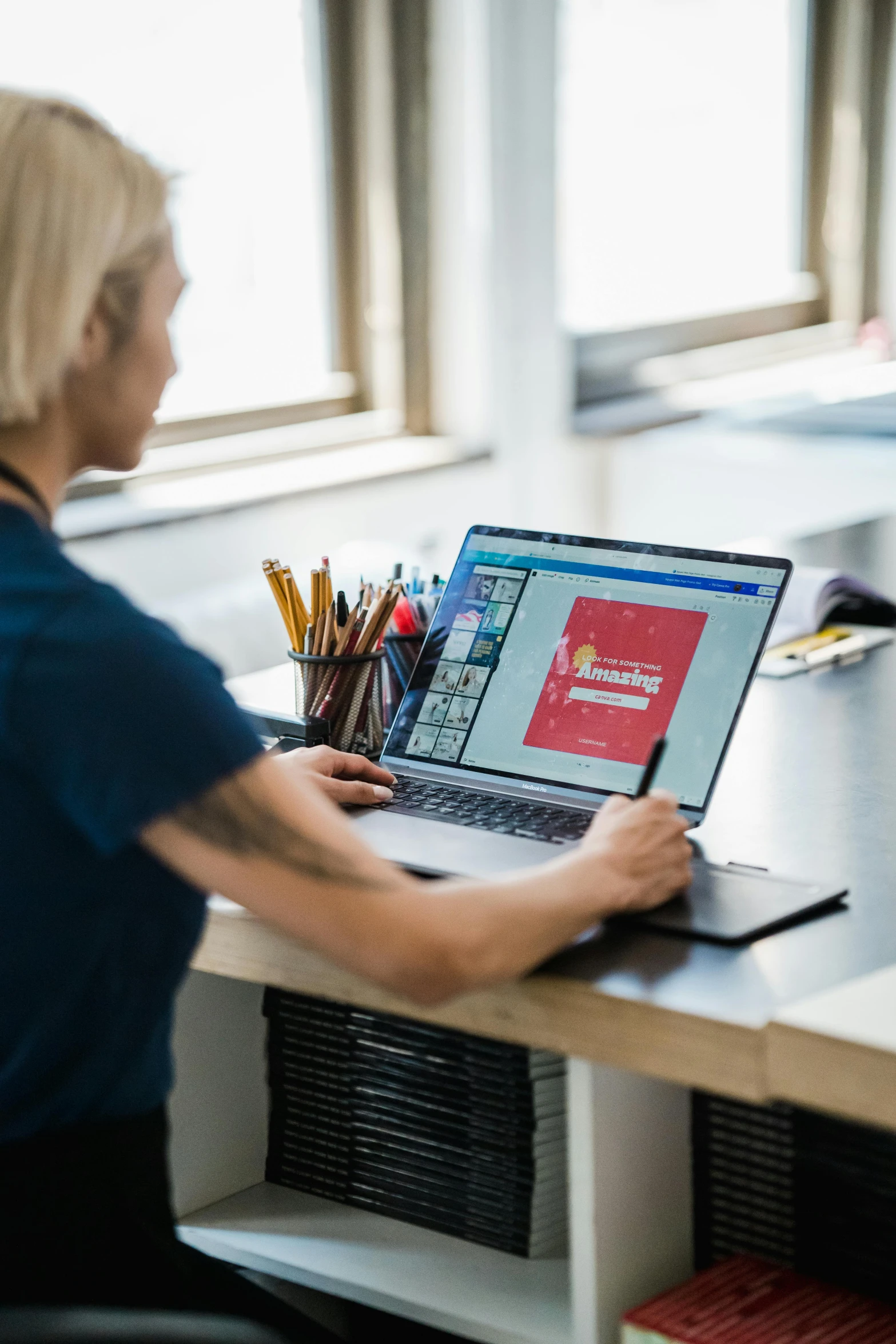 a person standing at a desk with a lap top and pencils