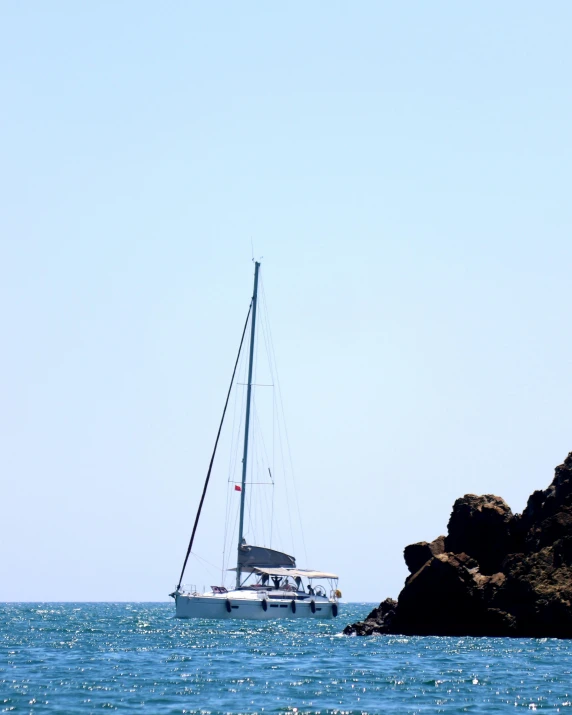 a sailboat traveling on open water near a rocky outcropping