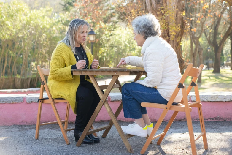 two elderly women playing chess outside on an asphalt path