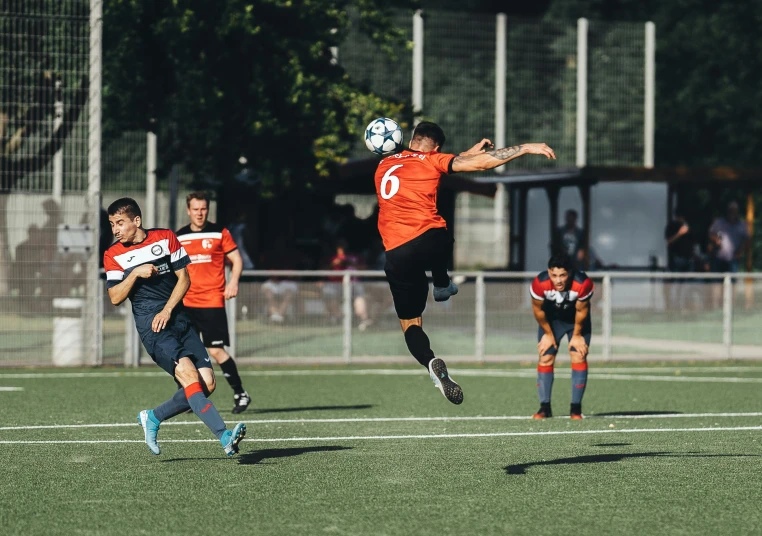 a person wearing orange jumping into the air to kick a soccer ball