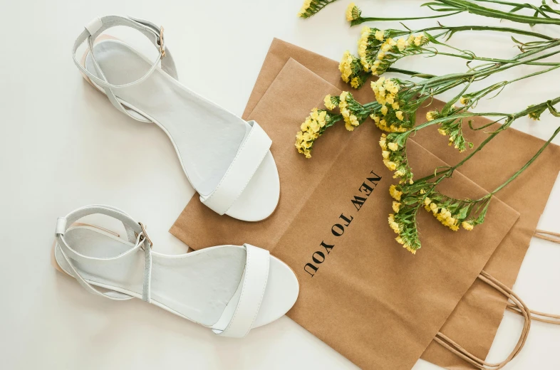 a pair of white sandals laying on a brown bag