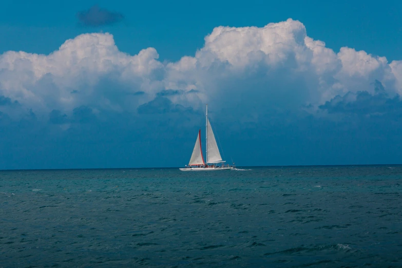 a small sailboat in the ocean under cloudy skies