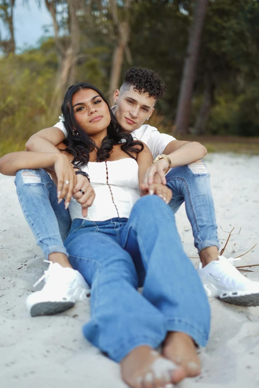a young man and woman sit on the beach together