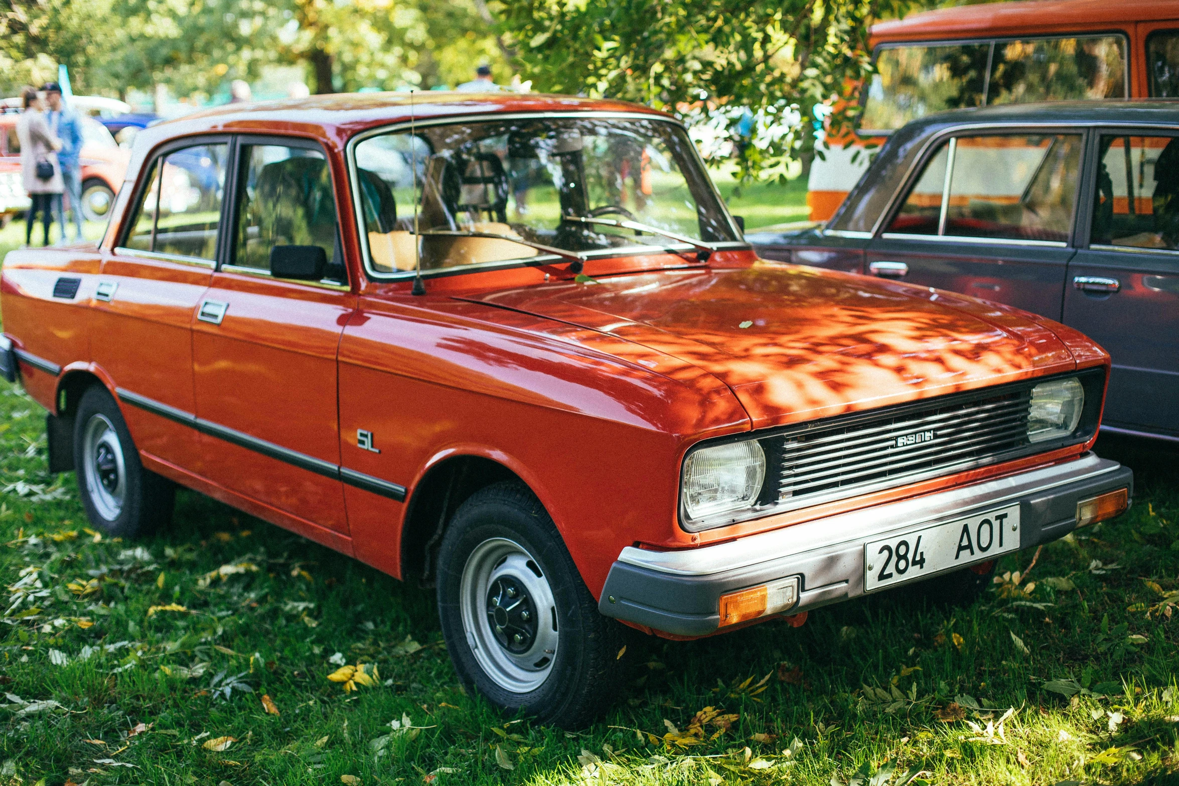 an orange car parked next to another vehicle in the grass