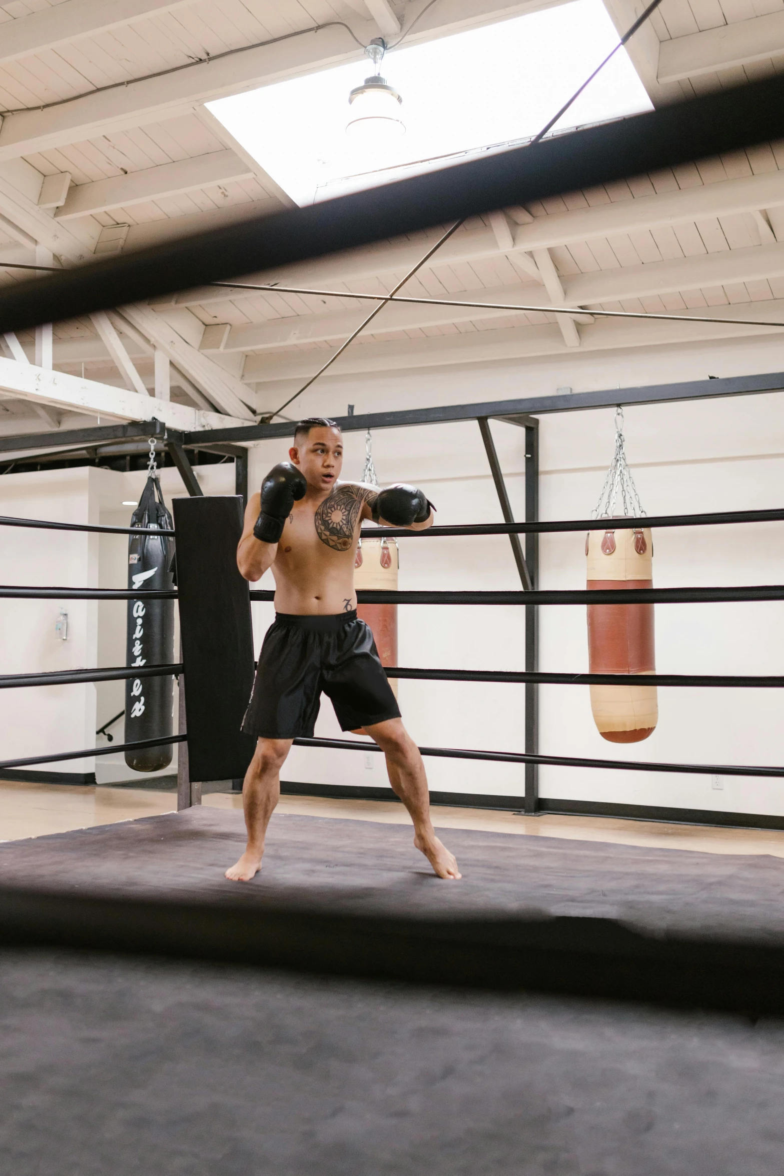 a shirtless man wearing boxing gear in the ring with a punching bag