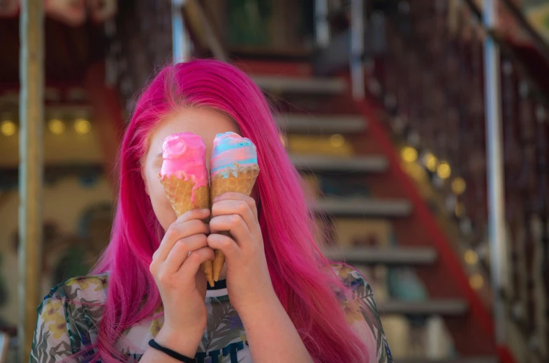 a girl holding two pink ice creams in front of her face