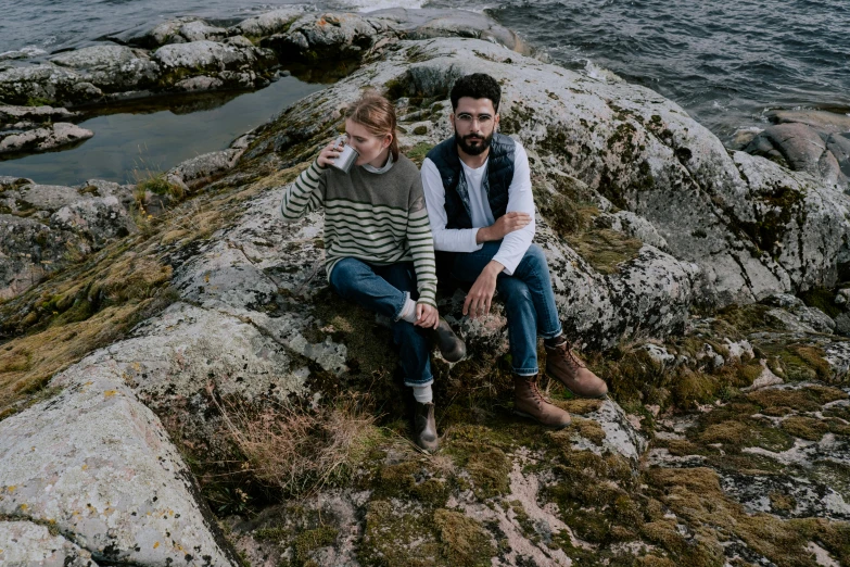 a woman is sitting on top of a rock while she holds a man's hand