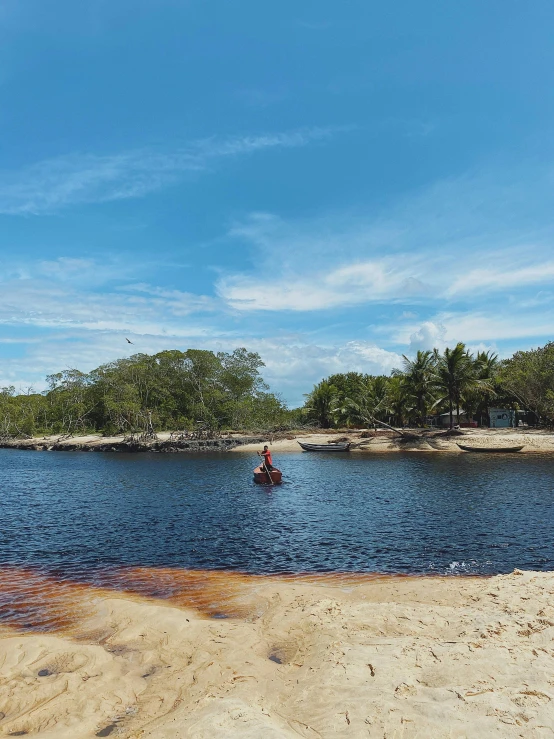 a man on a kayak rides along a sandy shoreline near an island