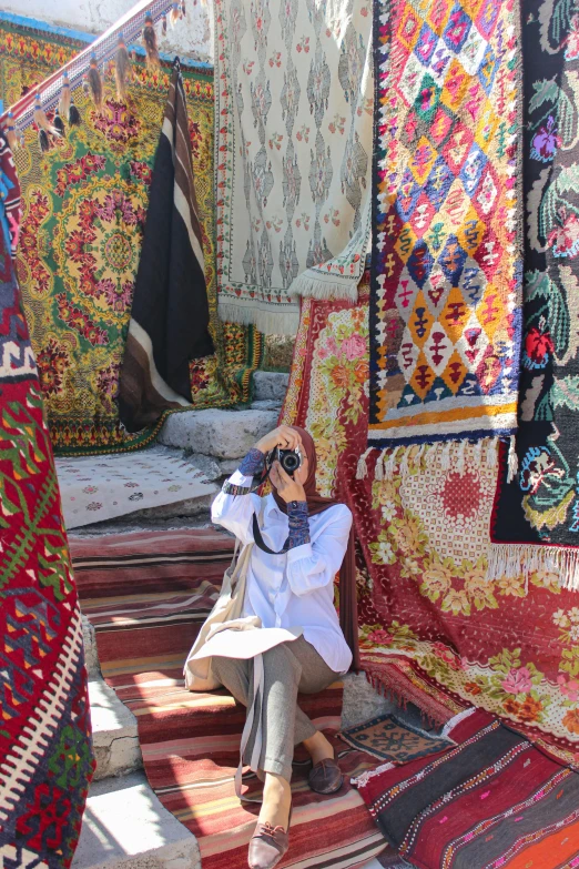 the woman is sitting under the fabrics, and taking a picture