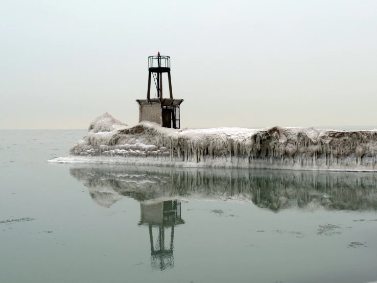 a tower stands on the water in front of ice covered shore