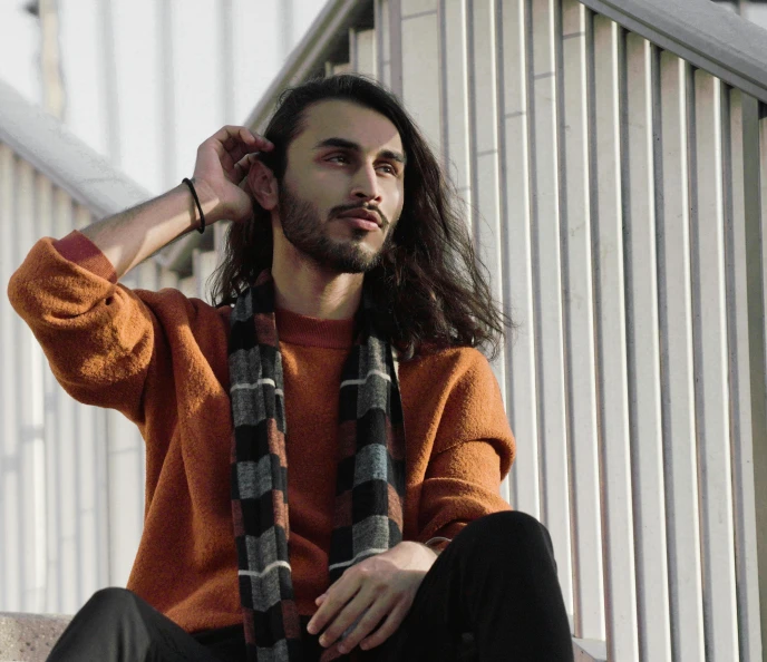 a young man wearing an orange sweater and long scarna