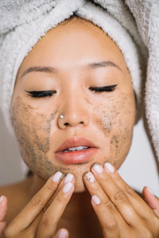 a young woman with a white towel on her head has a black spot on her face and hands underneath the head