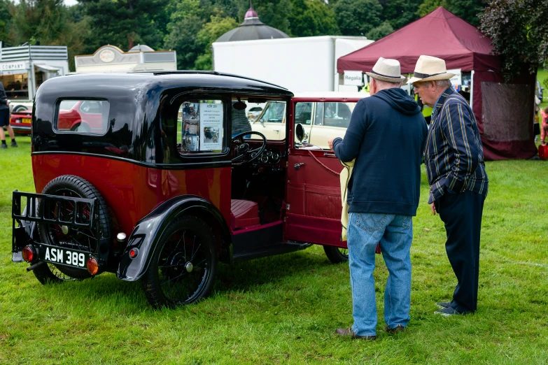 two men looking at an old style red car