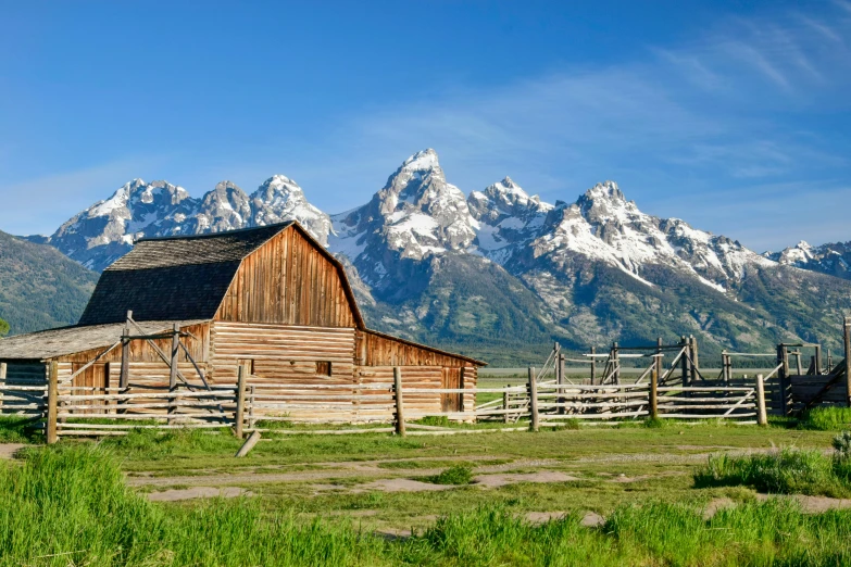 an old farm in front of mountains with a fence