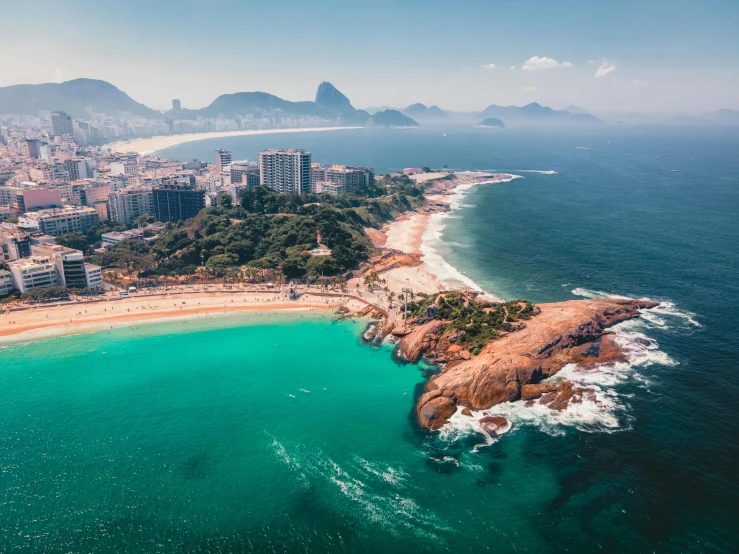 the coast has clear blue water, a city and large mountains in the background