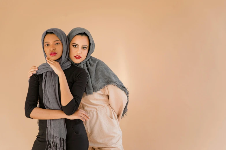 two women standing together in scarves with a tan background