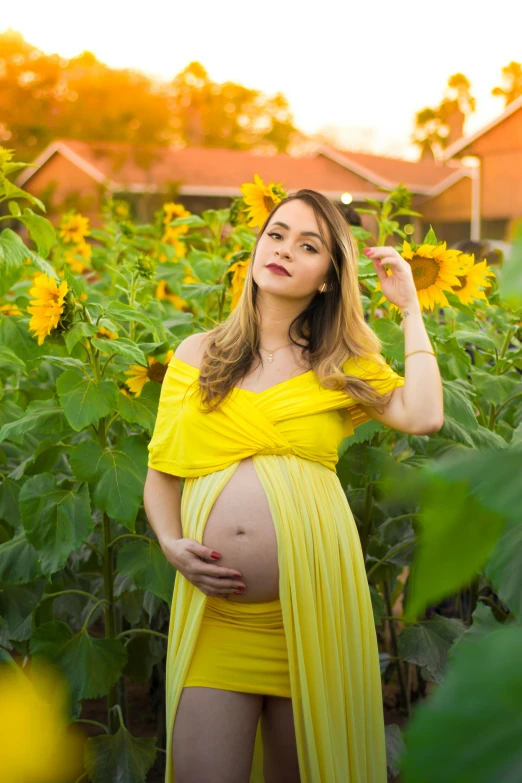 a pregnant woman standing in a field with yellow flowers