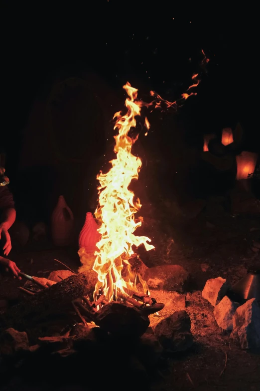 a fire burns in the dark with two people next to it