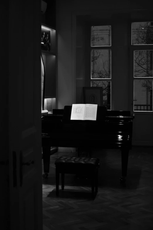 a piano in a darkened room with two windows