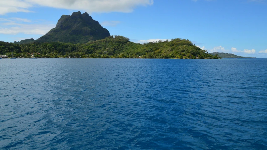 an island is behind the water with trees on the shore