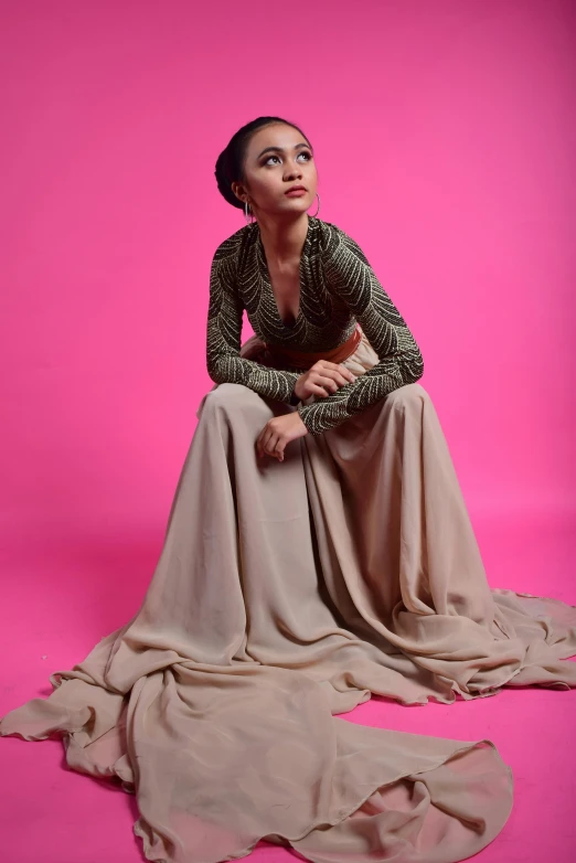 a woman sitting on a pink ground in a long dress