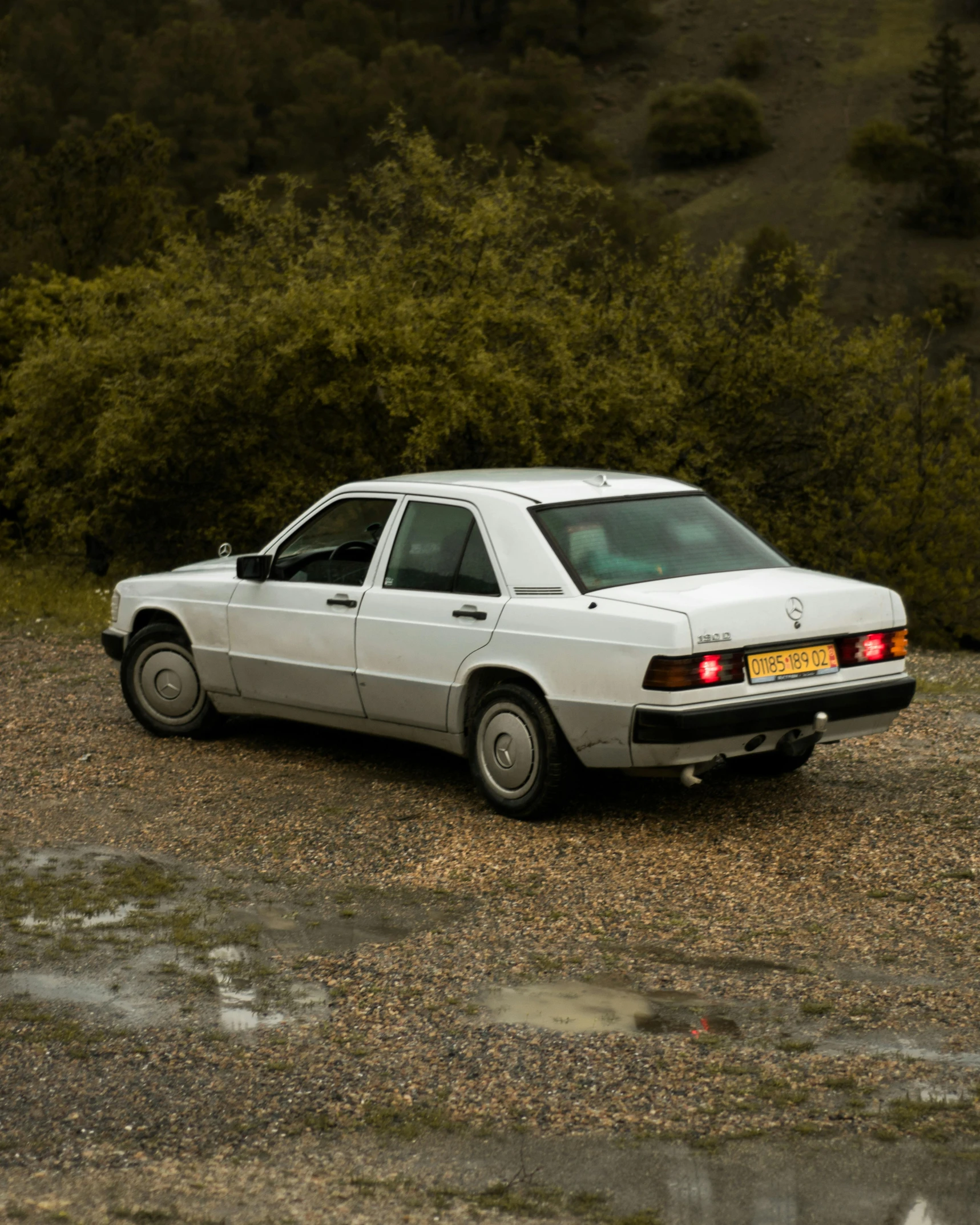 the white car is parked on the gravel