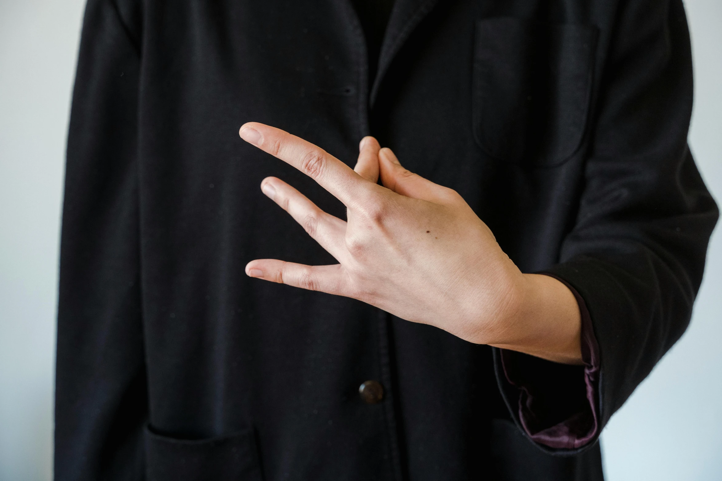 man in black coat making a sign with his hand