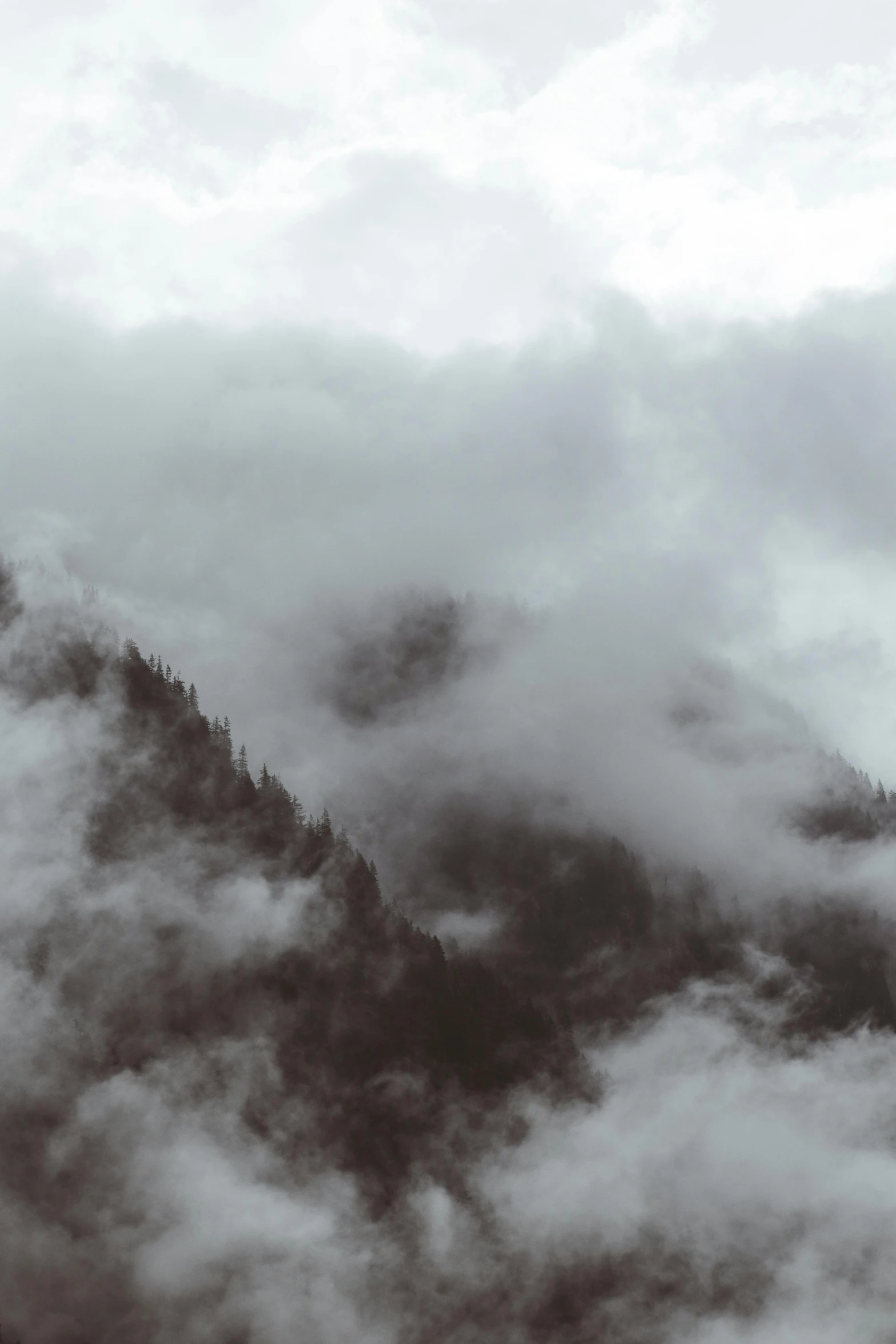 a mountain shroud by clouds as it rises above the ground