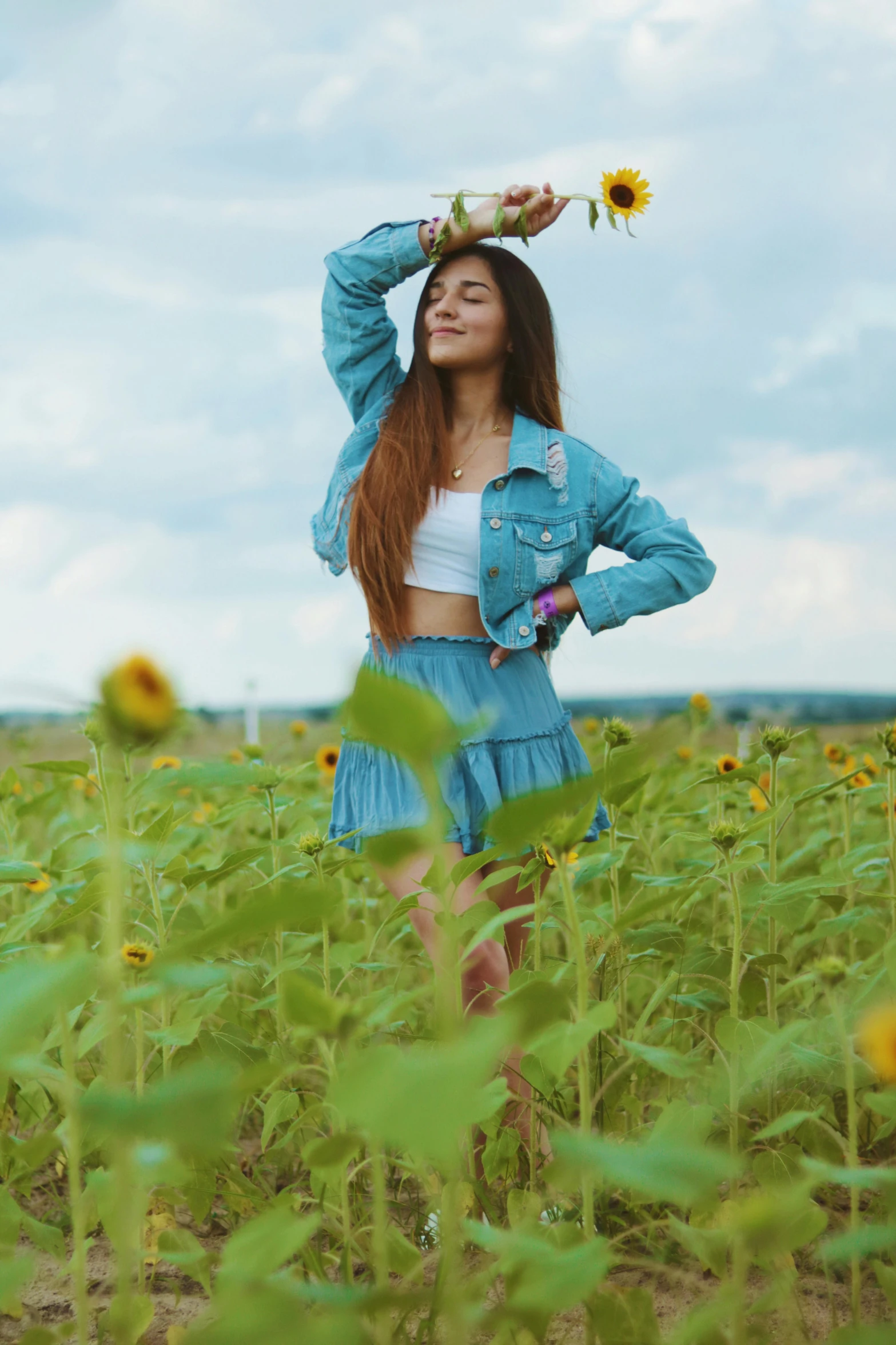 young woman in a sunflower field wearing a denim jacket and sunflower crown