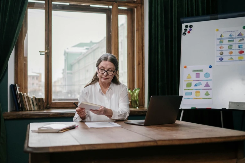 woman sitting at table reading book with a laptop in the middle