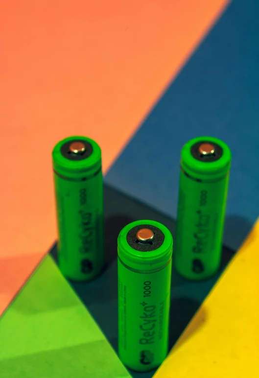 three batteries in green sitting on top of a multicolored backdrop