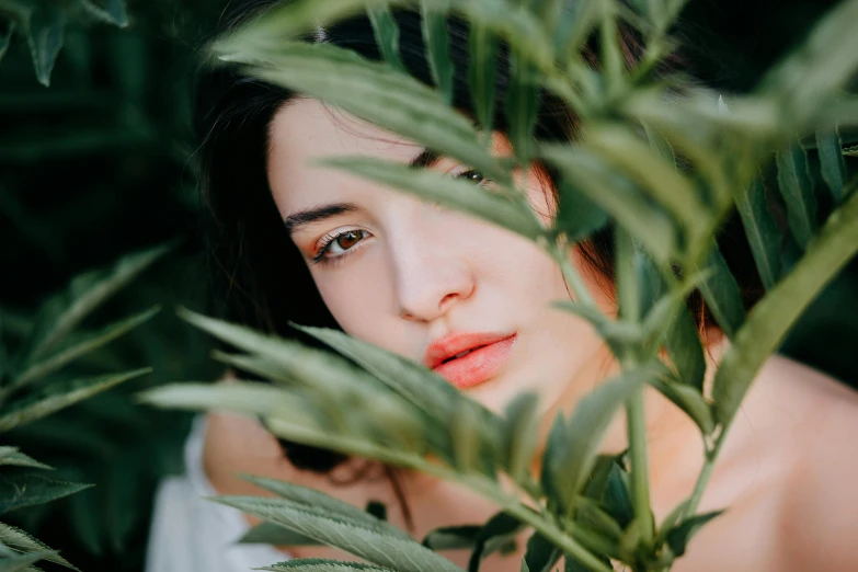 an asian woman wearing a white top surrounded by green leaves