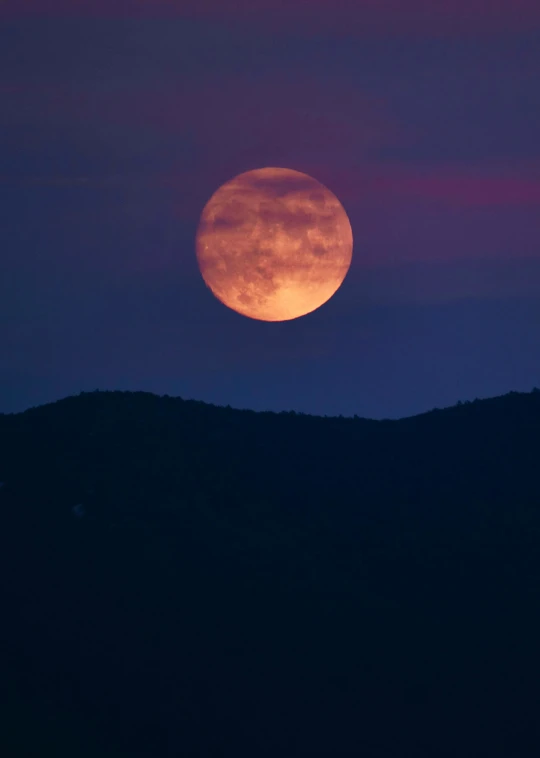 a moon rising over the mountains as seen from the ground