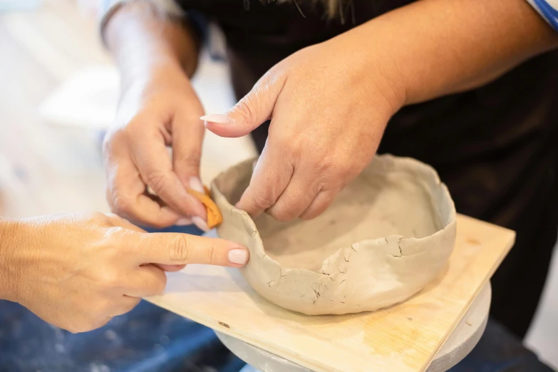 someone uses a small knife to shape a pottery bowl