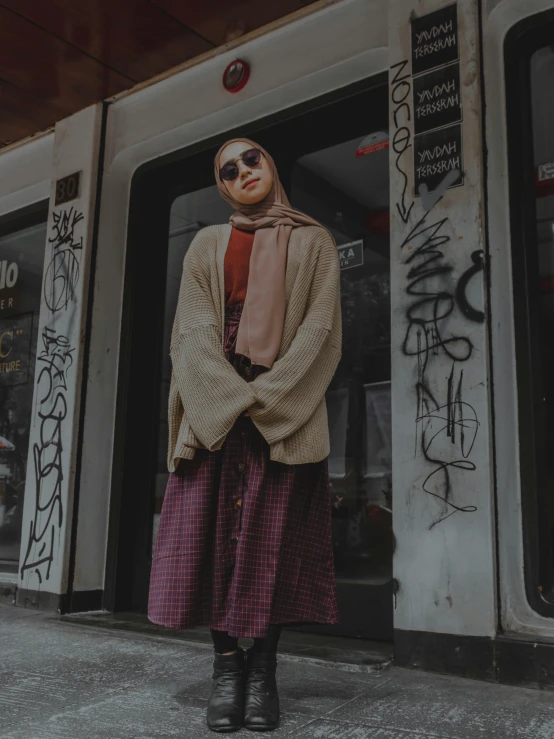 a woman in sunglasses and a scarf standing in front of a store