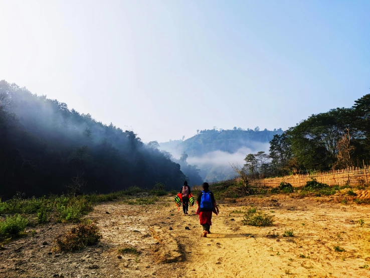 three people walking up a dirt trail in a wooded area