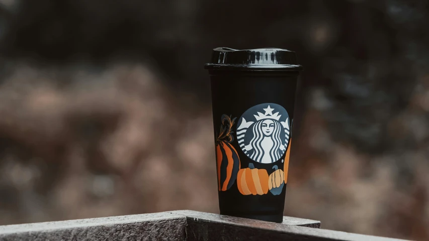 a starbucks cup on a cement surface with a pumpkin and cat