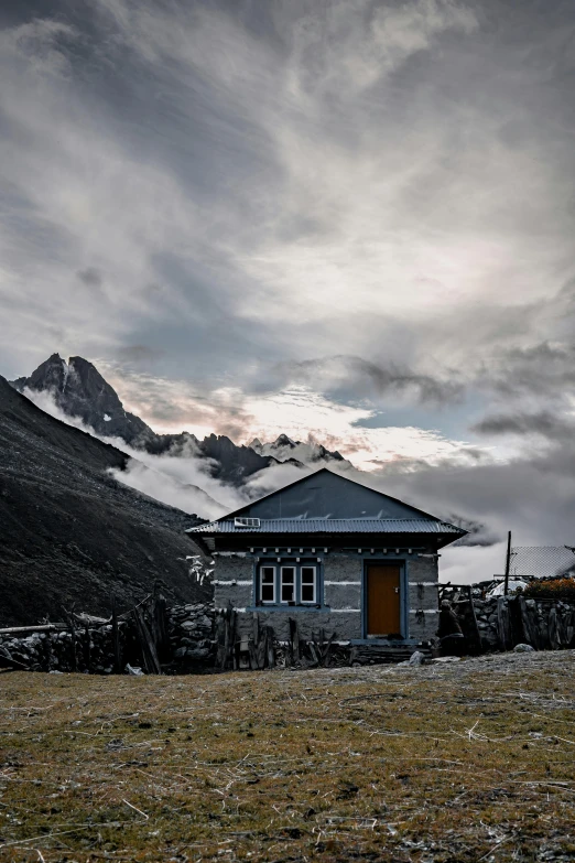 old, rundown house near a mountain slope under cloudy skies