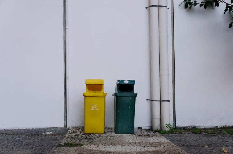 two waste bins are sitting outside against a white wall