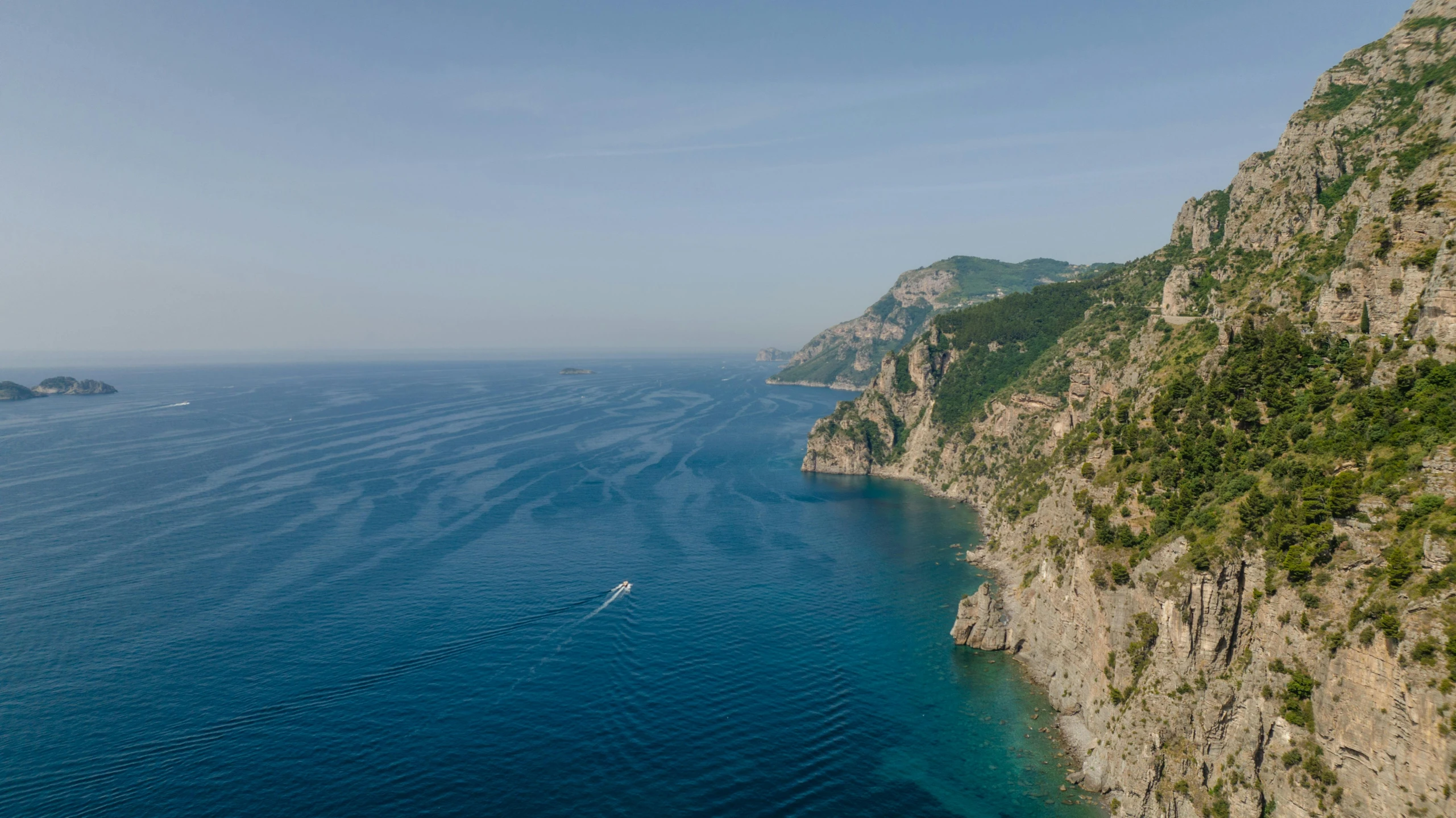 a boat in the blue water near a hill and some hills