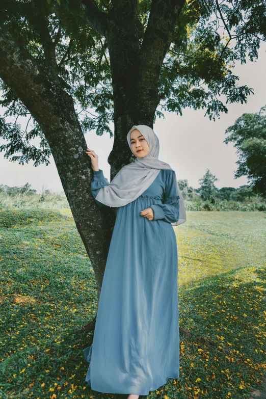 a young woman posing next to a large tree