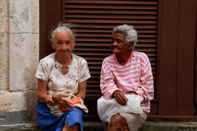 two elderly people sit on a bench by a wall